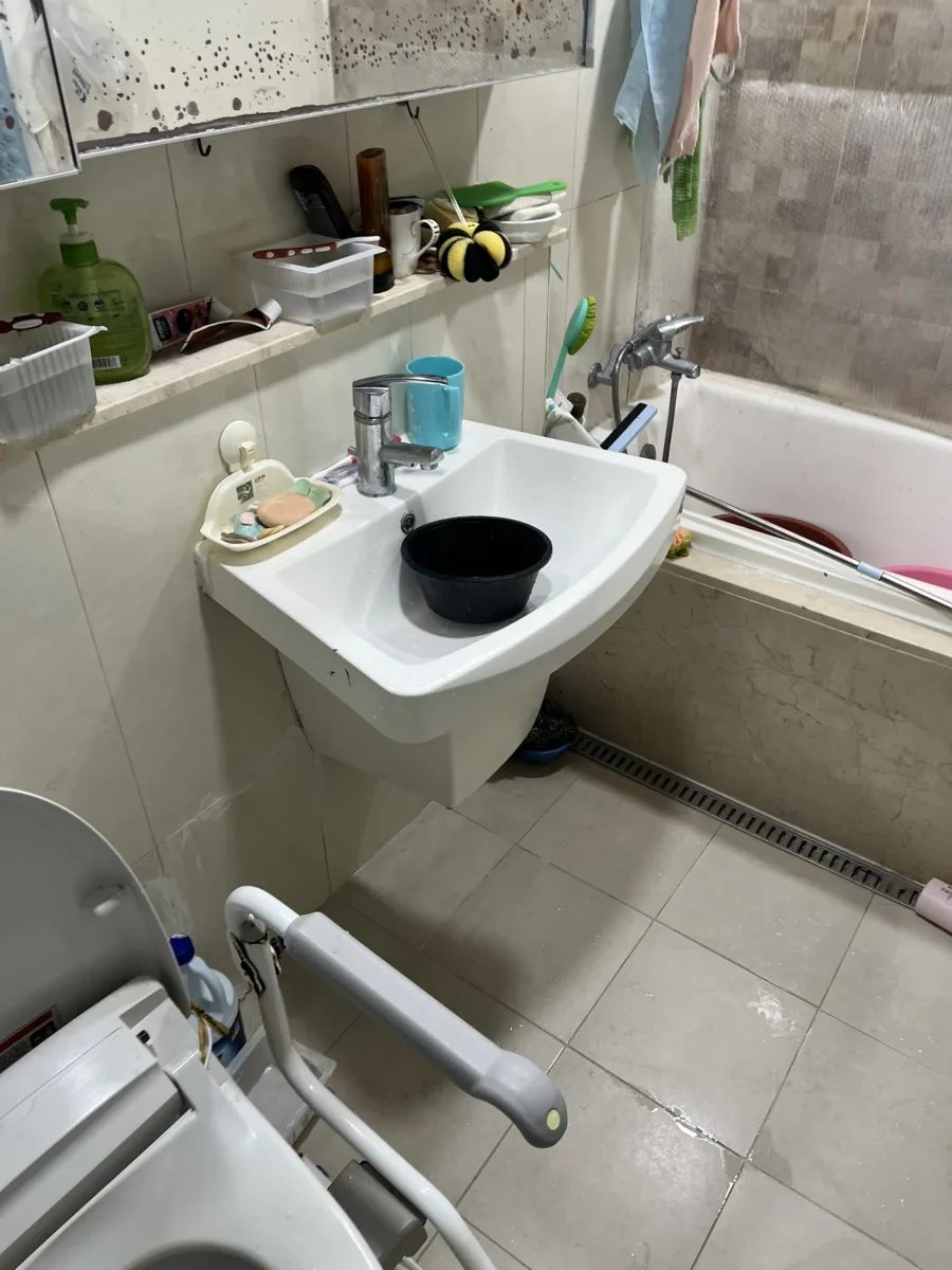 벽걸이형 세면대와 거울 선반 주변에 안전손잡이가 없는 욕실 시공 전 모습