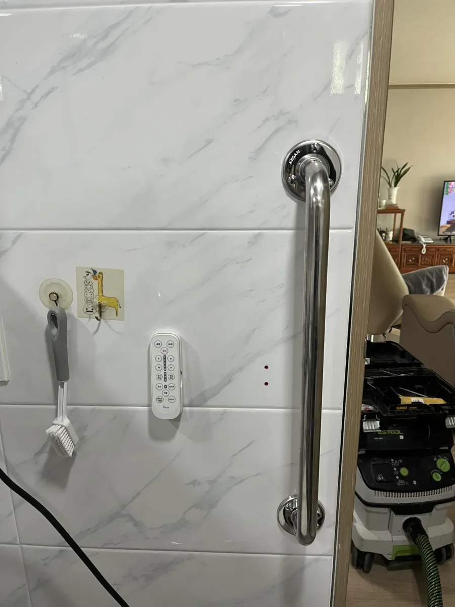 욕실 문 옆 대리석 무늬 타일 벽에 수직 손잡이를 설치한 모습 설치 부위